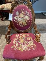 Front view showing carved wood frame and floral needlepoint upholstery on seat and back.