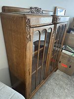 Side angled view showing carved wooden details, glass doors with vertical wood trim, and cabinet wood grain finish.