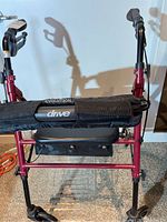 Front view showing red frame, padded black seat, cushioned backrest, and hand brake labeled handles.