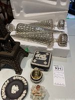 Overall lot photo showing metal Eiffel Tower candleholder, 3 silver glass Christmas decorations in styrofoam packing, Wedgwood trinket box, Jasperware plate, lidded jar and ballerina figurine.