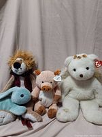 Four assorted stuffed toys sitting against a plain beige backdrop: lion, dolphin, pig, and bear.