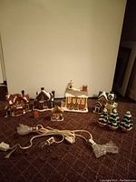 Photo of six ceramic Christmas village houses lined against a wall with string lights laid in front.
