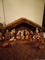 Nativity scene showing the assembled creche with figurines including Holy Family, angel, and Three Wise Men along with animals in front, placed on carpet.