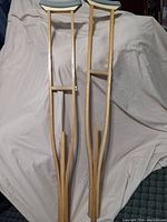 Pair of adjustable wooden adult crutches standing upright showing their full length, padding, and adjustment mechanisms.