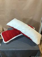 Two long rectangular throw pillows, one leaning against the other showing contrasting red knit front and white plush back.