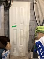 Full view of white paneled door leaning against wall with various household items nearby