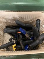 Photo of multiple hand clamps with black handles in white plastic bin