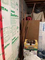 Photo showing several straight copper pipes leaning against a wall beside boxes and foam insulation boards.