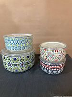 Front view of five stoneware covered dishes arranged in two stacks showing distinct colorful patterns.