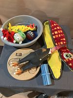Photo of various colorful dog toys including plush squeaky toys and a wooden interactive puzzle toy with parts on a table.