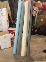 Five rolls of seamless paper backdrops held upright in a basement or storage room setting.