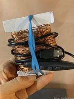 Copper wire USB powered fairy lights wrapped around a white card with inline button control and USB plug shown. Held in hand to show size and detail.