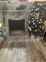 Shows the full vinyl Christmas backdrop with a fireplace and Christmas tree on a wood floor print, held up by a person to illustrate size and details.
