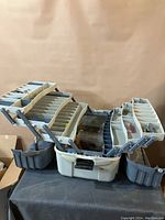 Photo of open, multi-tiered plastic fishing tackle box showing multiple empty and some filled compartments