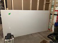 Large whiteboard resting against an unfinished interior wall in a storage space. Board clean but with signs of wear.
