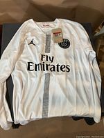 Front view of white PSG soccer jersey with Fly Emirates sponsor and Jordan brand logo.
