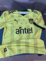 Front view of yellow Puma jersey showing tonal stripes, Puma logo, Antel sponsor