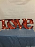 Front view of red metal light up sign spelling 'Love' with lights turned on