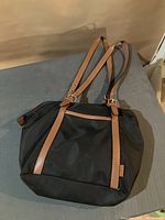 Front and top view of black nylon Roots purse with brown leather straps and buckle details, showing its shape and design.