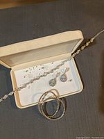 Full set of jewelry displayed in a beige box including a crystal necklace, bracelet, and earrings. Some small crystals visibly loose on the box surface.