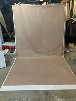 Full view of tan vinyl backdrop held vertically showing its length and width dimensions, with white edging on sides.