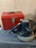 Metal toolbox with handle and latch, red in color, shown closed with electric buffer placed in front