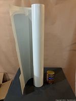 Full view of the white vinyl roll standing upright beside a small can of beans for size reference.