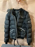 Front view of black Guess women's puffer jacket size medium showing zipper, pockets and fur-lined hood.
