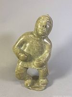 Front view of Inuit soapstone carving showing figure holding ball and detailed face.