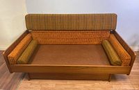 Front view of walnut veneer daybed with orange and green plaid upholstered cushions for back and sides, showing the wooden frame and cushions fitting inside it.