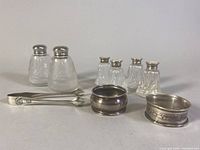 Full group photo of sterling silver sugar cube tongs, two napkin rings, and three sets of salt and pepper shakers.