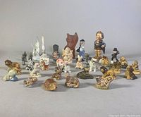 Full view of the collection of 27 assorted miniature figurines on a light surface including animals, humans, and metal pieces.