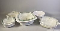 Overview photo showing a group of five vintage CorningWare casserole dishes with four glass lids, showcasing various sizes and patterns.
