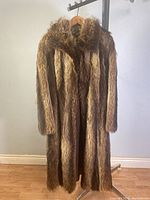 Front view of the vintage ladies raccoon fur coat hanging on a rack, showing the furry texture and length.