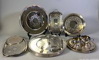 Full display of silver plated servingware including 13 inch chargers, rectangular trays, creamer, sugar bowl, and matching trays.