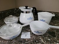 Photo showing full set of Corningware including large teapot, measuring cup, and cookware pieces on marble counter.