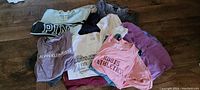 Lot of ladies' t-shirts laid out, showing different brand logos and colors, including Pink, Calvin Klein Jeans, and Roots Athletics.