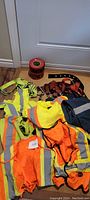 Various reflective workwear items including high-visibility vests, shirts, safety belts, and caution tape arranged on floor.