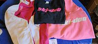 Three Ski-Doo apparel items: pink sweatshirt, black and pink long sleeve shirt, pink and white zip-up sweatshirt.