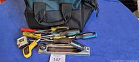 Photo of black tool bag with multiple hand tools arranged in front including screwdrivers, measuring tape, and wood plane.