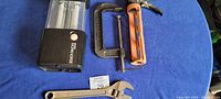 Photo showing all four items together on blue fabric: work light, orange caulking tool, black C-clamp, and Craftsman wrench.
