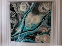 Front view of the square resin wall art showing abstract teal and white textured circular designs within a white frame.