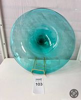 Front view of a large teal blue glass bowl displayed on a stand, showing its wide rim and concave center.