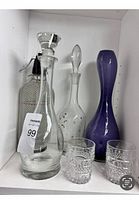 Shelf display with two glass decanters, vintage steel mesh covered seltzer bottle with black siphon top, two etched lead crystal glasses, and a tall purple art glass vase.