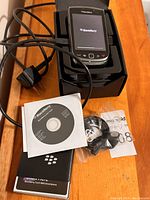 Photo of BlackBerry Torch 9800 smartphone in cradle with charging cable, user manual, and software installation CD.