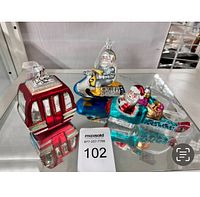 Group photo of three larger Christmas ornaments: red gondola, Santa astronaut on snowmobile, and Santa in rocket ship
