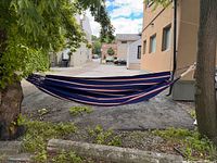 Photo of Hatteras two-person hanging hammock set up between trees outdoors, blue canvas with colored stripes visible.