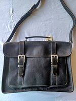 Front view showing black pebble leather texture, two buckle straps, and adjustable shoulder strap.