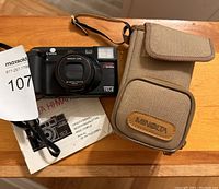 Minolta Hi-Matic AF camera on table with original travel case and user manual, showing front view of case and camera.