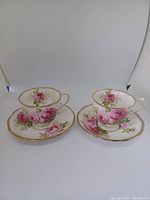 Two sets of Royal Albert American Beauty teacups and saucers displayed showing front view of porcelain and floral designs with gold trim.